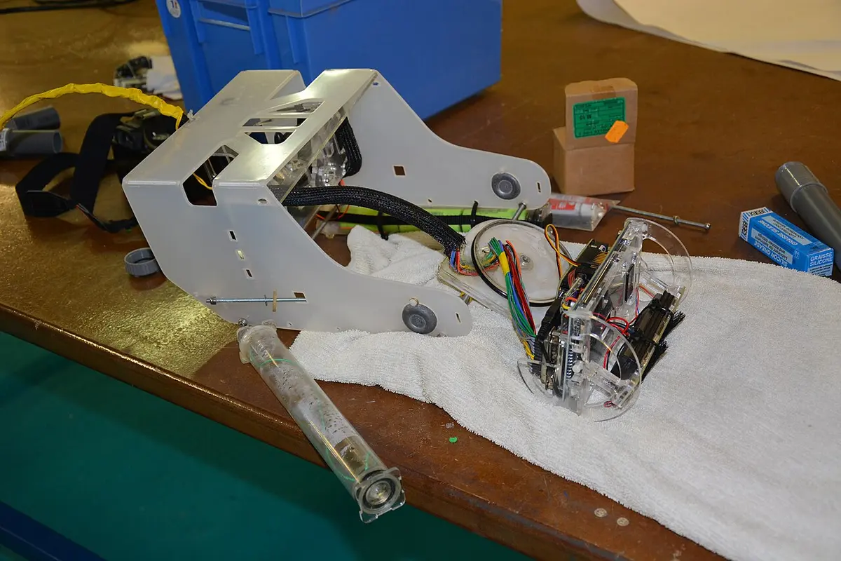 Halb montiertes OpenROV auf einer Werkbank: weißer Kunststoffrahmen, offene Acrylröhre mit Platinen und bunten Kabeln, daneben Werkzeug